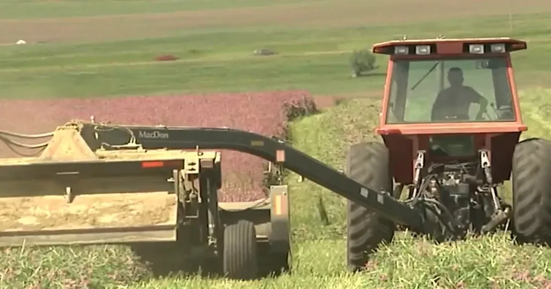 A tractor and farm equipment moving along a rural Michigan road during harvest season